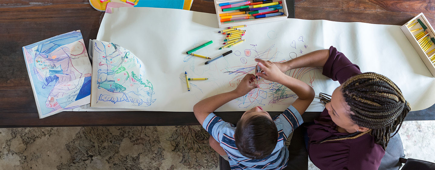 overhead photo of student and teacher sitting next to each other and coloring on a roll of paper