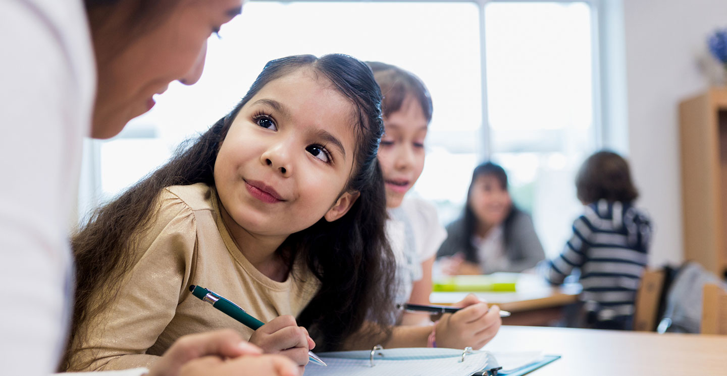 student sitting at desk and looking at her teacher