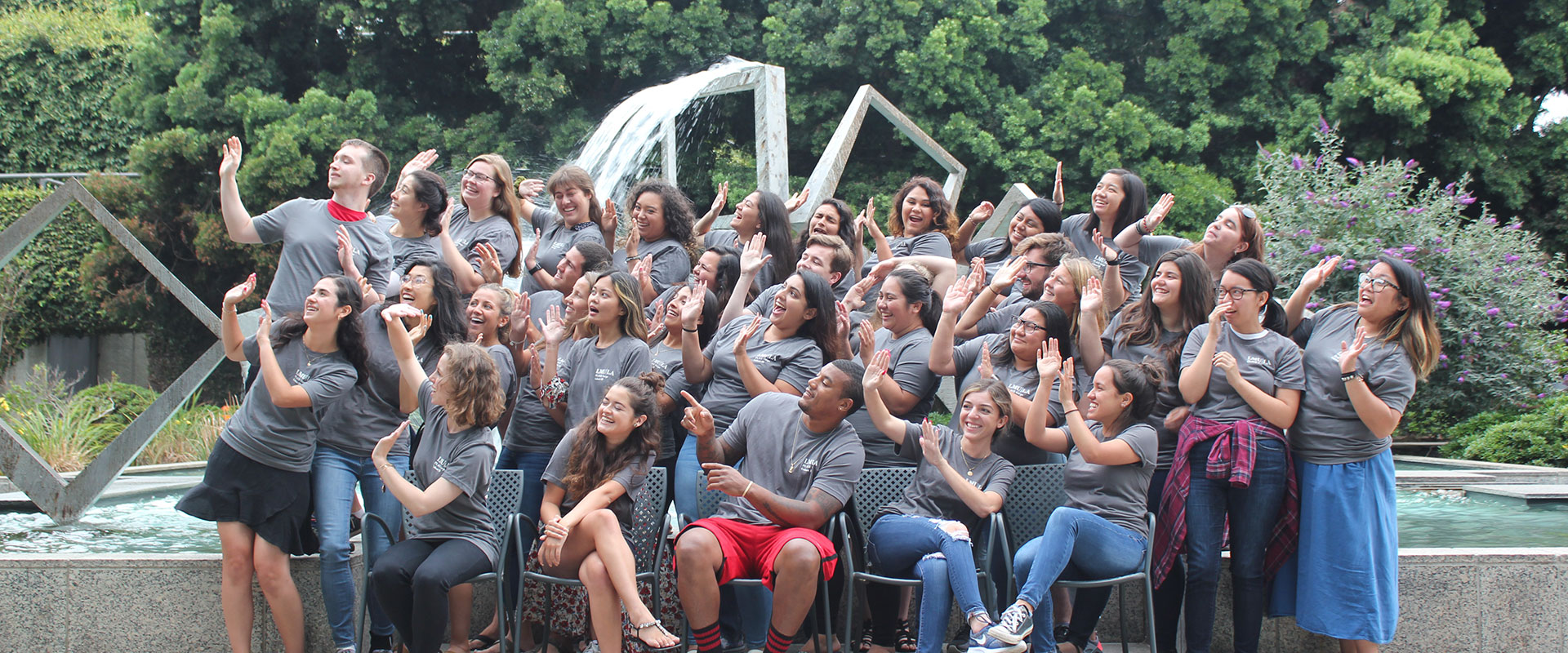 A large group of PLACE students in a funny photo in front of the fountains on Shea Terrace