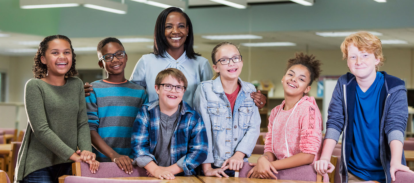 teacher and students in a classroom smiling at the camera