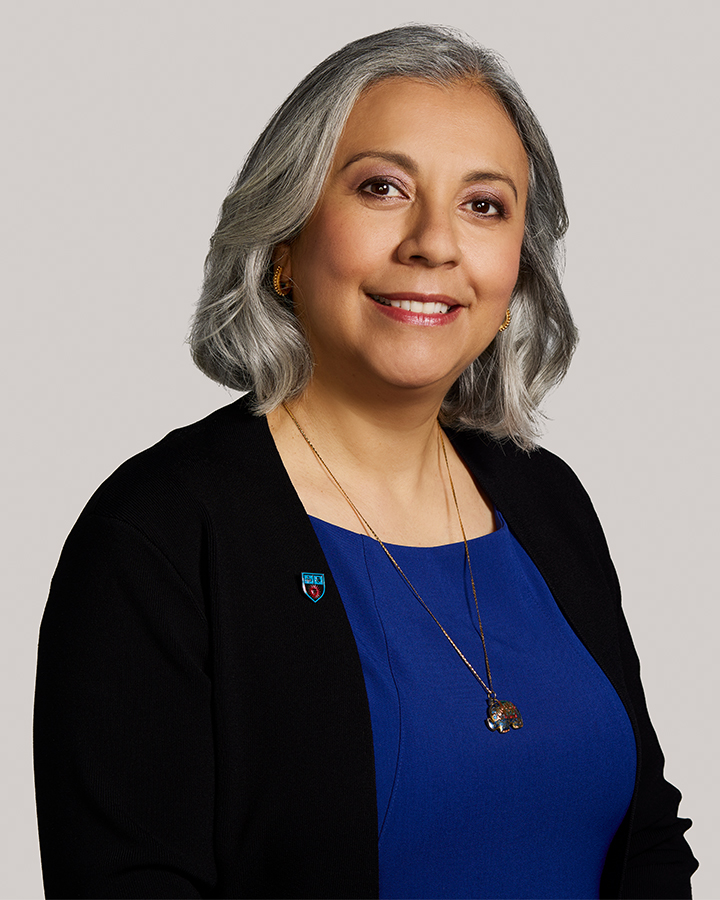 Estela Zarate Portrait with blue shirt and black sweater, and a grey background