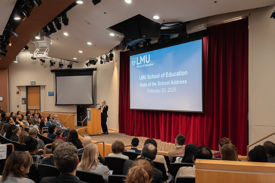woman standing at a lectern and next to a large presentation screen in an auditorium