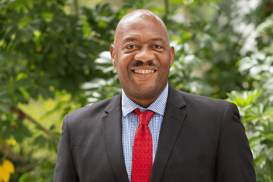 man in a blue suit and red tie standing in front of greenery and trees