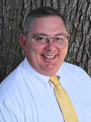 Man in white shirt and yellow tie posing in front of a tree trunk