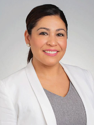 Karla Estrada Portrait woman with dark hair in white blazer posing in front of a white background