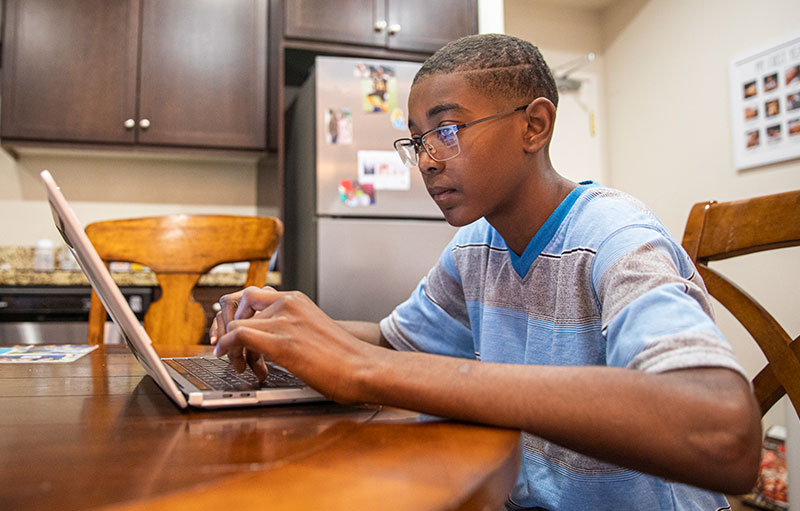 middle-school aged Black boy works on laptop at kitchen table